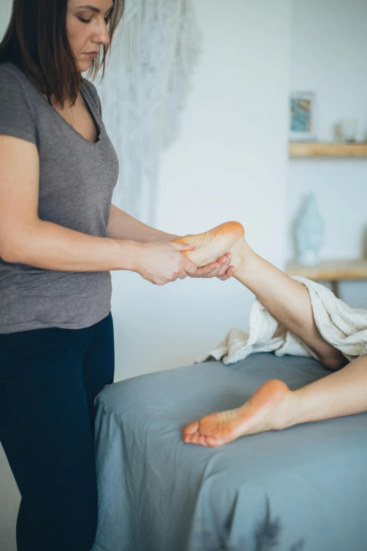 a woman getting a foot massage in a room, bending down slightly, laurie greasely, thumbnail, uncrop