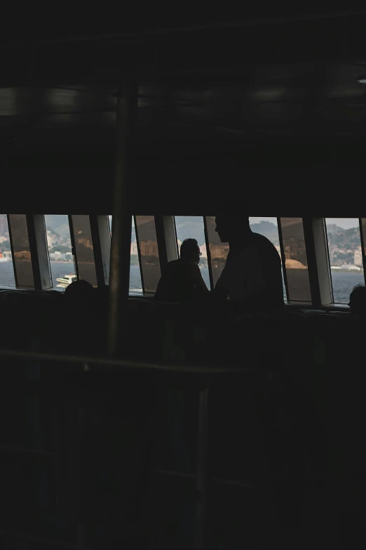 a group of people standing in front of a window, interior of staten island ferry, shadowy and dark, cockpit view, two people