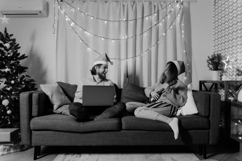 a man and woman sitting on a couch in front of a christmas tree, a black and white photo, pexels, figuration libre, elves sitting on the couch, with a laptop on his lap, in a japanese apartment, wearing a party hat