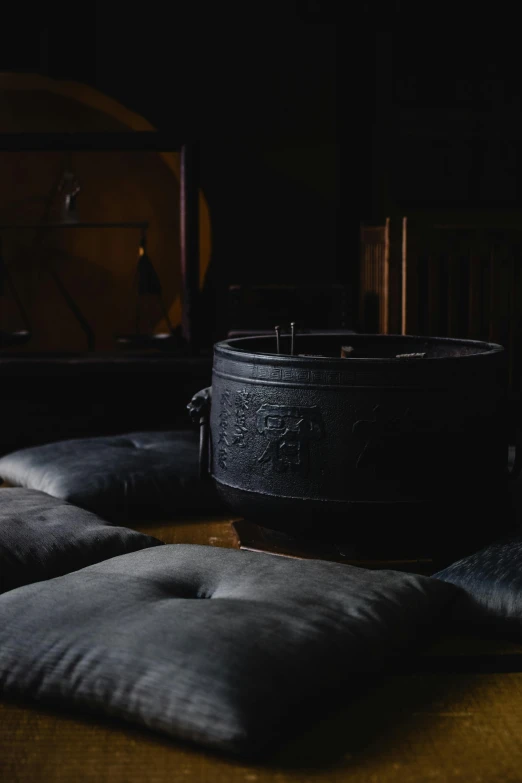 a black pot sitting on top of a wooden table, an album cover, inspired by Inshō Dōmoto, trending on unsplash, rustic throne room, steamed buns, dimly lit interior room, cushions