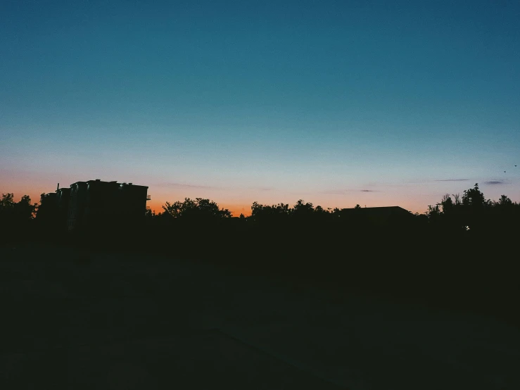 a silhouette of a building in the distance with trees in the foreground, a picture, inspired by Elsa Bleda, unsplash, postminimalism, blue sky at sunset, summer night, in a suburb, fades to the horizon