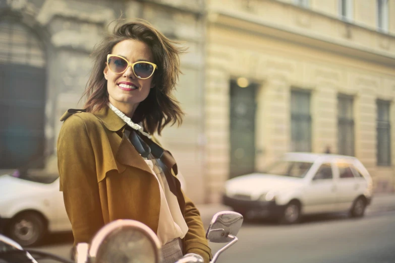 a woman riding on the back of a motorcycle down a street, pexels, wearing gold glasses, vintage colours, smiling fashion model, wearing trenchcoat