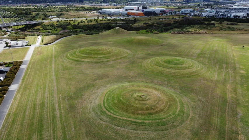 an aerial view of a large green field, a digital rendering, pexels contest winner, land art, round buildings in background, grassy knoll, te pae, many holes