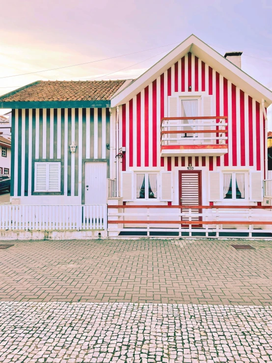 a red and white house sitting next to a white fence, a colorized photo, by Matija Jama, pexels contest winner, colorful striped pavillions, 🚿🗝📝, brazilian, wooden houses