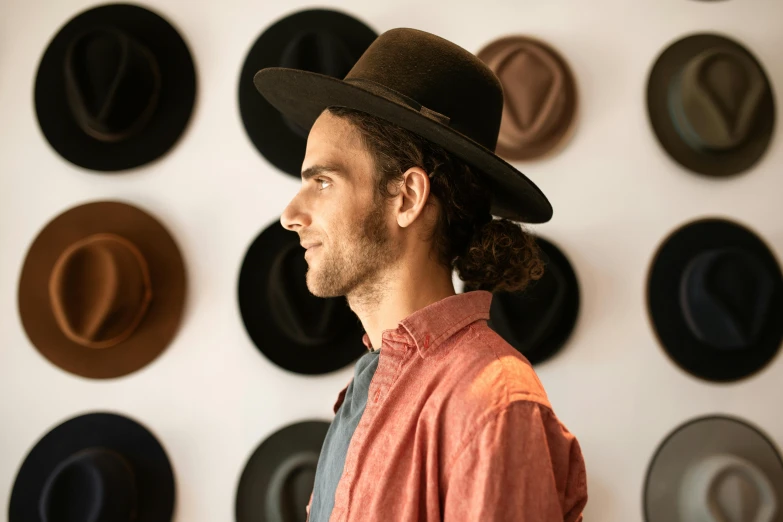 a man standing in front of a wall of hats, a portrait, by Meredith Dillman, unsplash, hozier, side profile waist up portrait, caracter with brown hat, detailed product shot