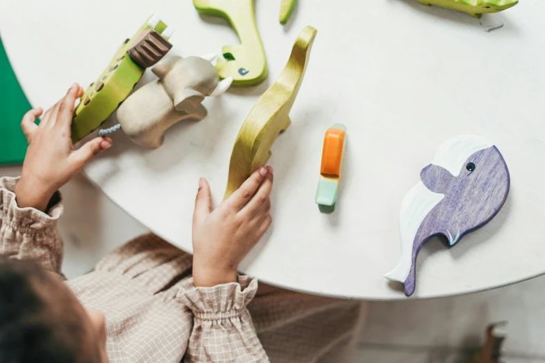 a child playing with wooden toys on a table, trending on pexels, painted pale yellow and green, flora and fauna, bending down slightly, organic forms