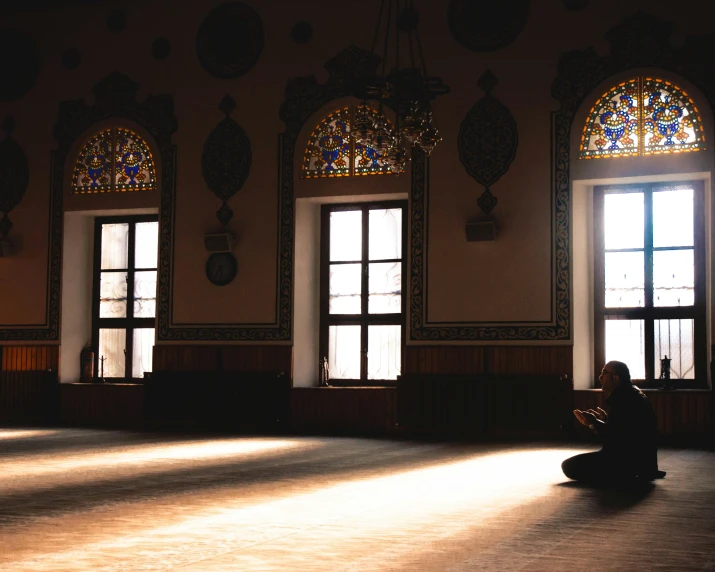 a person sitting on the floor in a large room, pexels contest winner, hurufiyya, prayer, orientalist, profile picture 1024px, with glowing windows