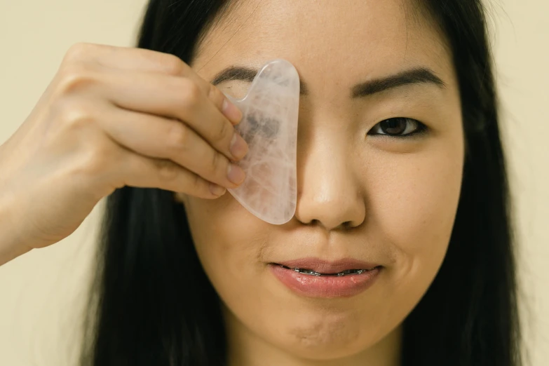 a woman holding a piece of ice over her eye, silicone patch design, asian features, wide forehead, jen atkin