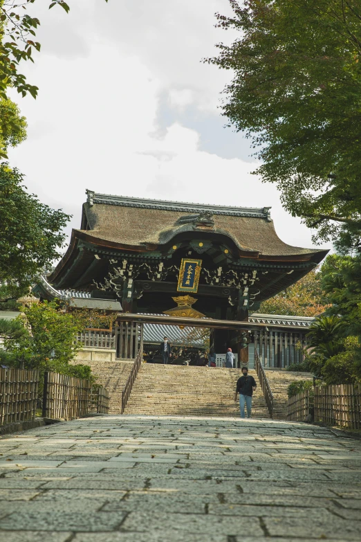 a couple of people that are standing in front of a building, inspired by Kanō Shōsenin, unsplash, sōsaku hanga, built on a steep hill, intricate detailed roof, covered outdoor stage, wide high angle view