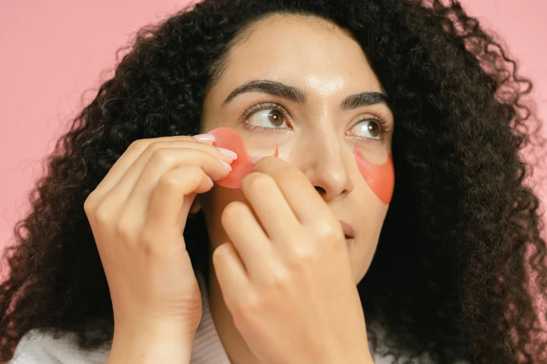 a woman putting makeup on her face, an album cover, trending on pexels, hurufiyya, eyepatches, pink and red color style, silicone skin, h3h3