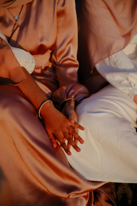 a woman sitting on top of a bed next to a baby, an album cover, trending on unsplash, romanticism, sitting with wrists together, brown skin, golden-white robes, her friend