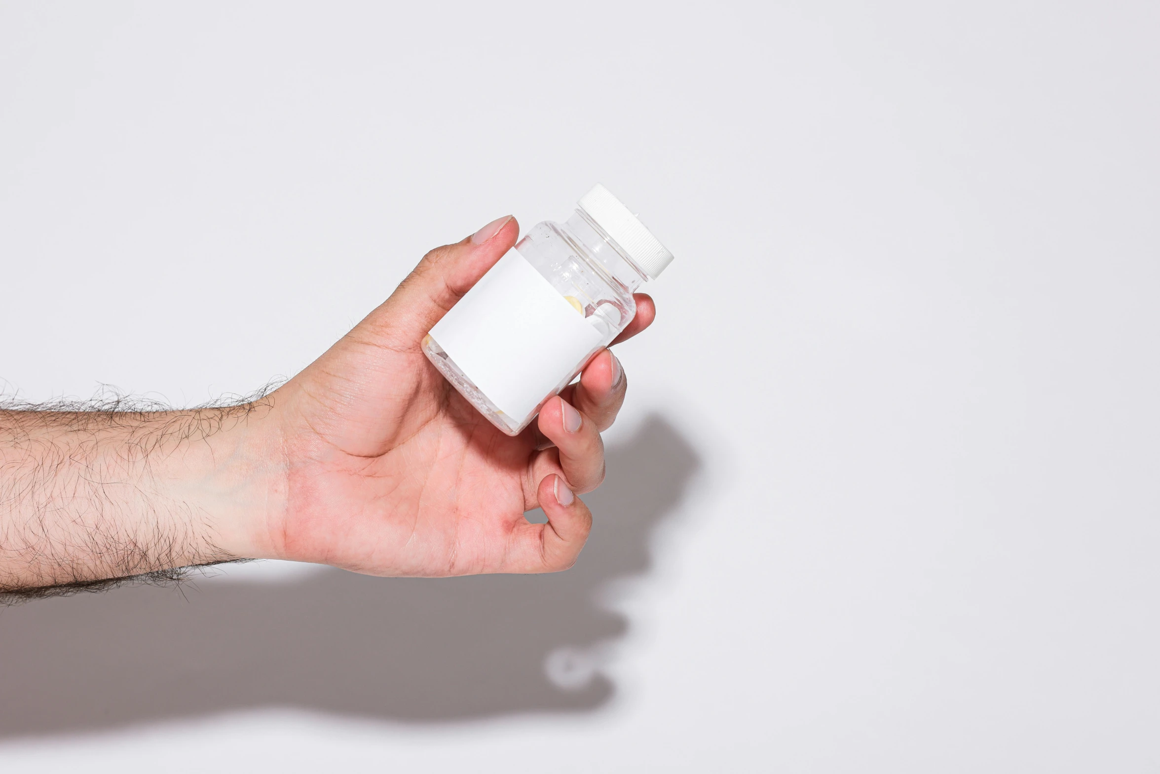 a hand holding a bottle of pills against a white background, by Adam Marczyński, unsplash, antipodeans, 3/4 front view, white porcelain skin, ignant, white male