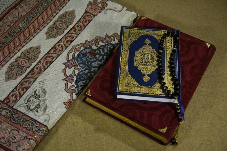 a couple of books sitting on top of a table, hurufiyya, rug, religious imagery, beige, religion