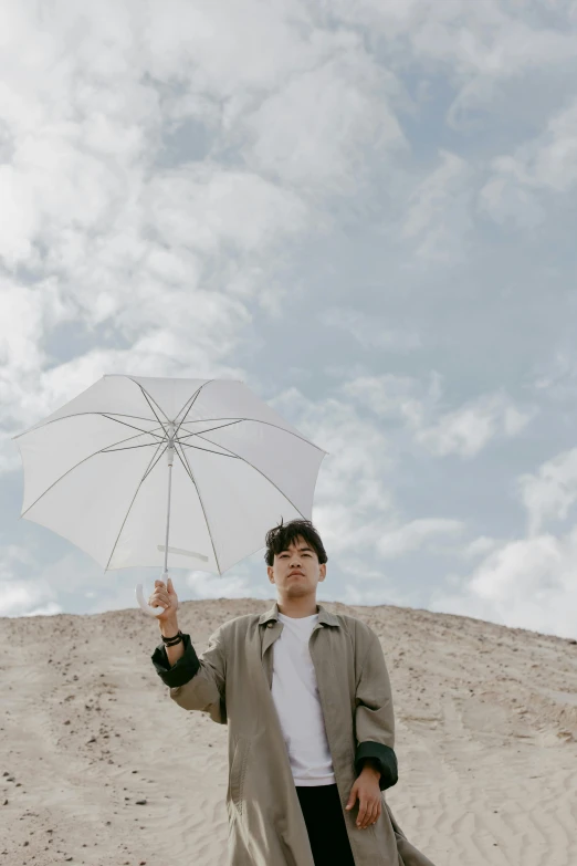 a man standing in the sand holding an umbrella, by Robbie Trevino, desert white greenhouse, in the sky, asian male, trending on vsco