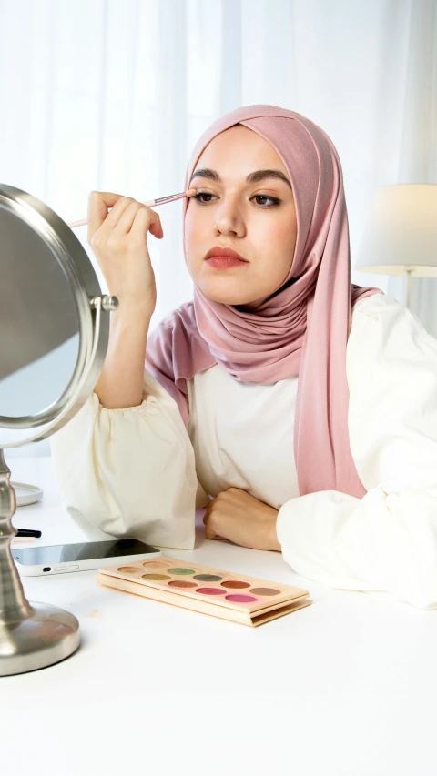 a woman sitting at a table in front of a mirror, a colorized photo, trending on pexels, hurufiyya, white hijab, pastel makeup, product introduction photo, thumbnail