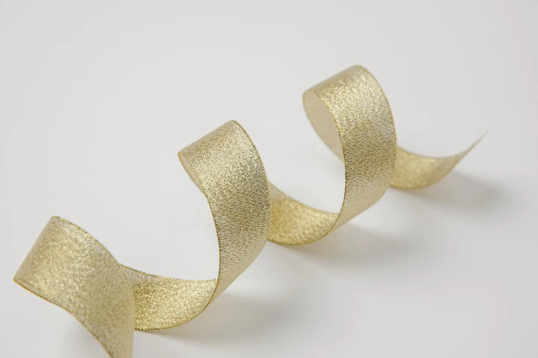 a pair of gold ribbon on a white surface, a stipple, inspired by Charles Angrand, trending on pexels, curved body, silver，ivory, birch, 1 8 mm wide shot