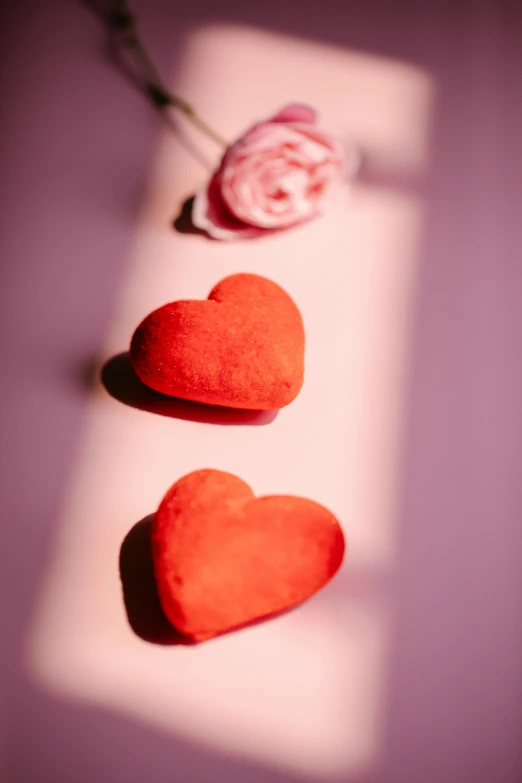 a couple of red hearts sitting on top of a table, pexels, with soft pink colors, romantic lead, dan mumfor, 1/320