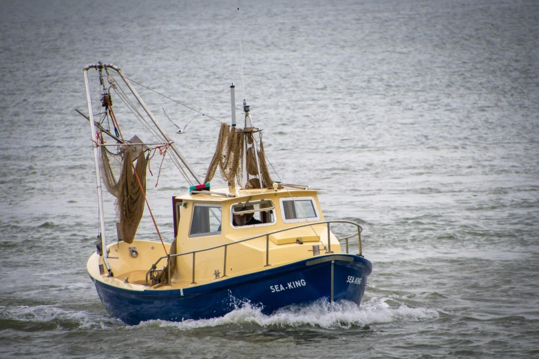 a blue and yellow boat traveling across a body of water, by Jesper Knudsen, pexels contest winner, fishing boat, replica model, ready to eat, offshore winds