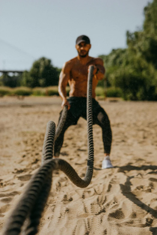 a man holding a rope on top of a sandy beach, wearing fitness gear, big snake, instagram story, gen z