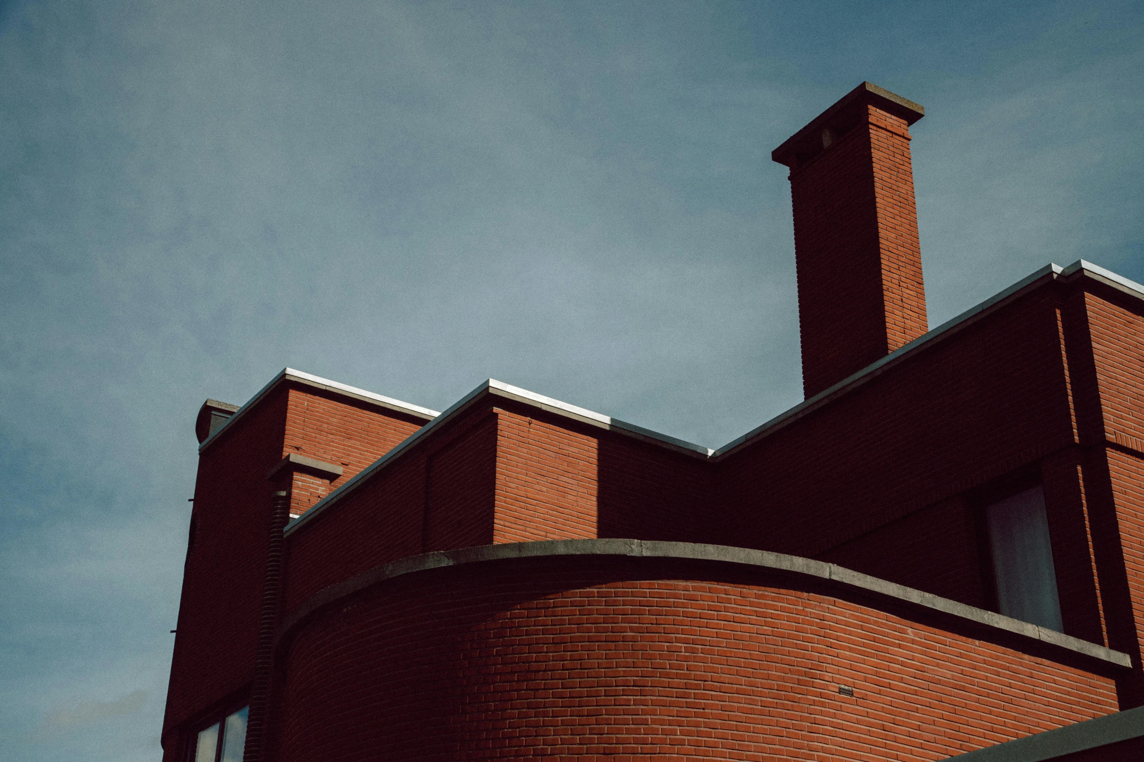 a red brick building with a clock on top of it, unsplash, brutalism, chimneys, flat curves, low quality photo, alvar aalto