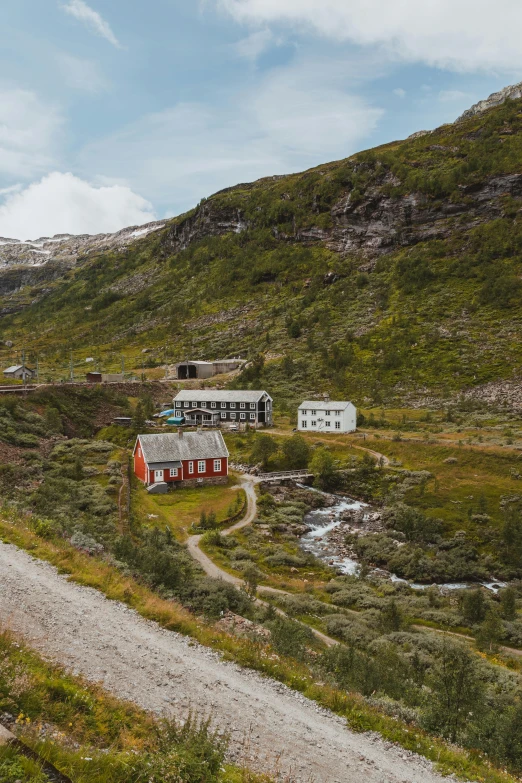 a red house sitting on top of a lush green hillside, by Roar Kjernstad, pexels contest winner, verdadism, rail tracks lead from the mine, whitewashed buildings, natural stone road, dark grey and orange colours