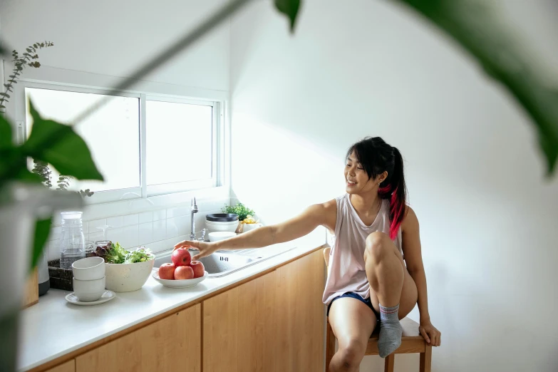 a woman sitting on a stool in a kitchen, inspired by Yuko Tatsushima, pexels contest winner, wearing a tank top and shorts, serving body, windowsill, profile image