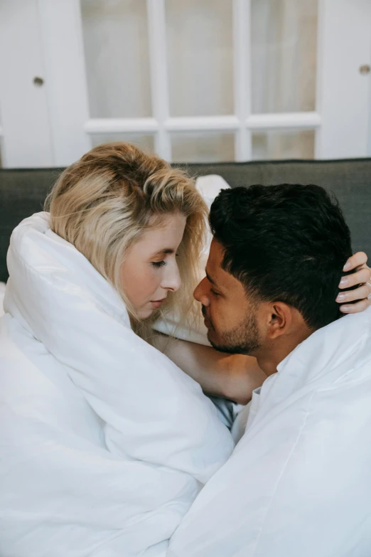 a man and woman laying in bed next to each other, trending on pexels, romanticism, arm around her neck, white robes, blonde woman, two men hugging