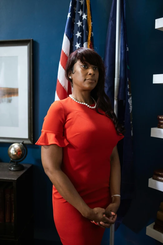 a woman in a red dress standing in front of an american flag, on a desk, atiba jefferson, conservative, looking serious