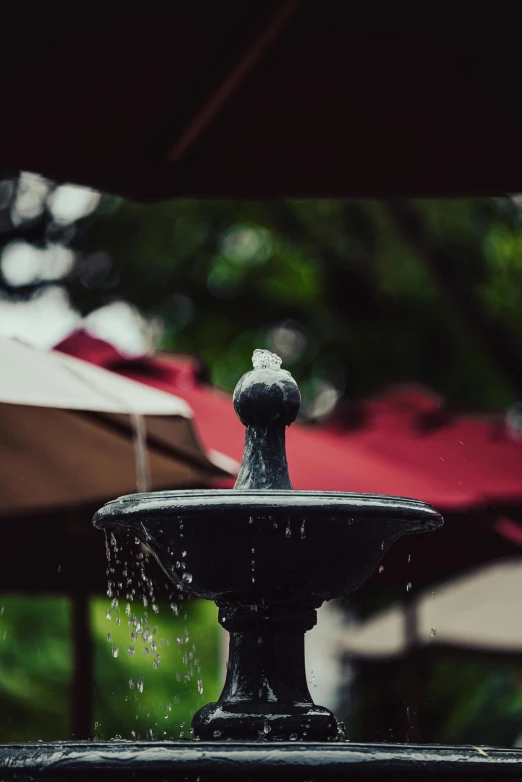 a close up of a fountain with umbrellas in the background, by Cherryl Fountain, unsplash, raining outside the cafe, small stature, detailed surroundings, half image