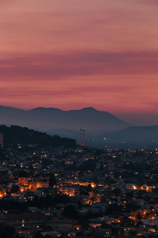 a view of a city at dusk with mountains in the background, by Dan Scott, unsplash contest winner, vallejo, pink hues, red hues, brown