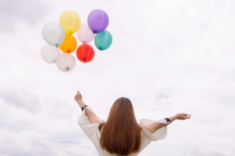 a woman holding a bunch of balloons in the air, a colorized photo, pexels contest winner, background image, minimalist photo, happy clouds behind, looking across the shoulder