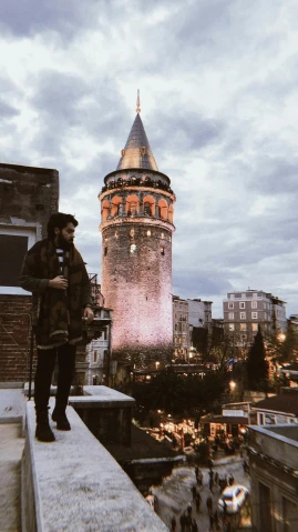 a man standing on top of a roof next to a tall tower, an album cover, by Niyazi Selimoglu, pexels contest winner, hurufiyya, zayn malik, ottoman sultan, instagram picture, thumbnail