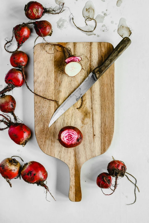 a wooden cutting board topped with beets and a knife, paddle and ball, natural point rose', multiple stories, image