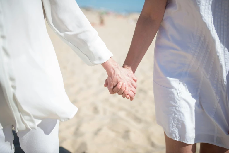 a man and a woman holding hands on a beach, by Arabella Rankin, unsplash, lesbian embrace, wearing white clothes, tournament, 15081959 21121991 01012000 4k