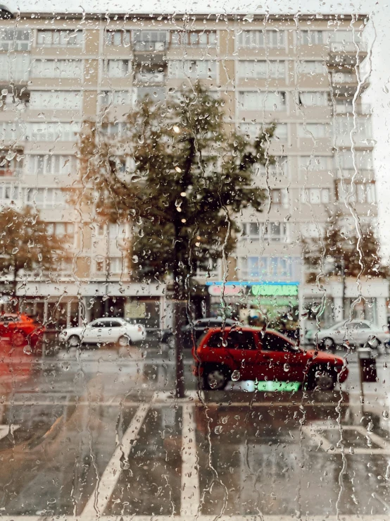 a red car driving down a street next to a tall building, a picture, inspired by Elsa Bleda, unsplash contest winner, hyperrealism, covered in water drops, gif, sovietwave aesthetic, window ( city )