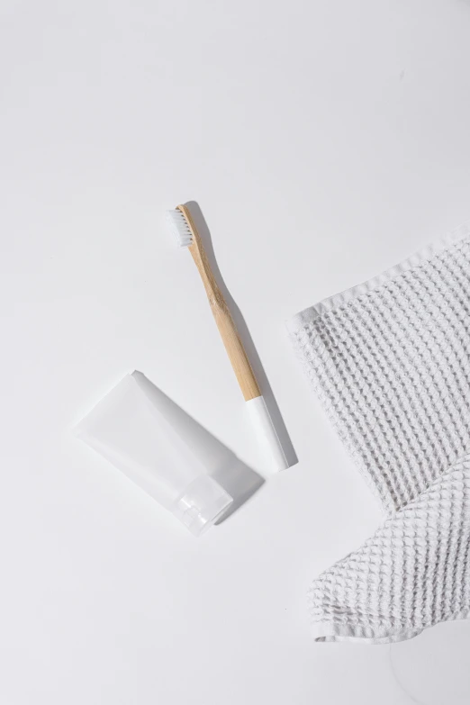 a toothbrush sitting on top of a towel next to a tube of toothpaste, made of bamboo, wearing white clothes, rectangle, product image