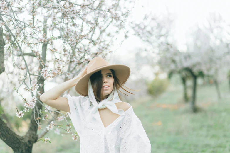 a woman standing next to a tree wearing a hat, pexels contest winner, persephone in spring, wearing a white shirt, brunette, white scarf