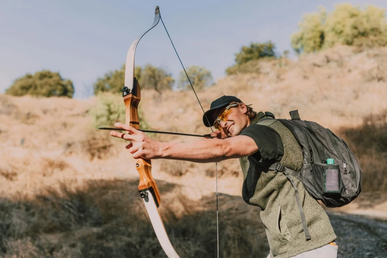 a man with a backpack holding a bow and arrow, pexels contest winner, camp, avatar image, angled shot, exterior shot