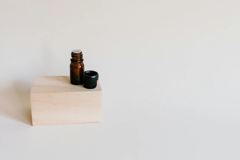 a bottle of essential oil sitting on top of a wooden block, by Emma Andijewska, minimalism, brown, small, vials, hyperminimalist