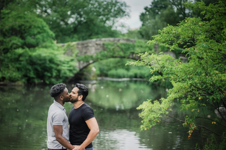 two men standing next to each other near a body of water, kissing, central park, riyahd cassiem, a quaint