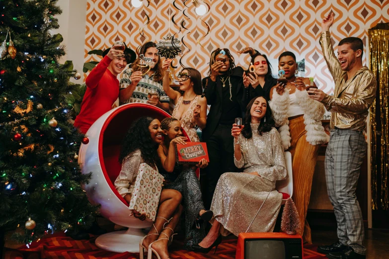 a group of people posing for a picture in front of a christmas tree, a photo, by Julia Pishtar, pexels contest winner, maximalism, 7 0 s vibe, champagne commercial, sitting on a throne, an olive skinned