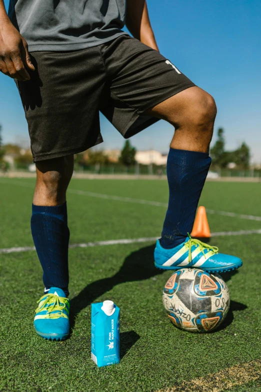 a man standing next to a soccer ball on a field, foot wraps, sprays, game ready, athletic shorts