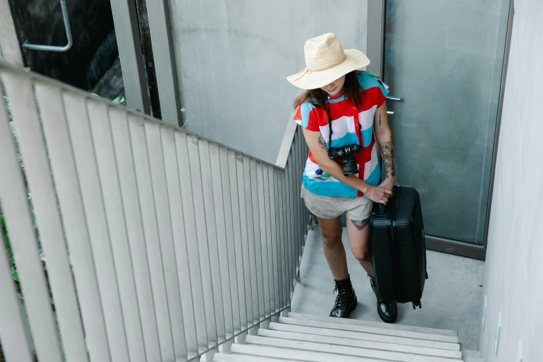 a woman carrying a suitcase down a flight of stairs, pexels contest winner, happening, baggy clothing and hat, lgbtq, in australia, maintenance