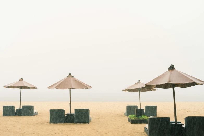 a group of umbrellas sitting on top of a sandy beach, unsplash, minimalism, foggy weather, zezhou chen, beach bar, shot on sony a 7