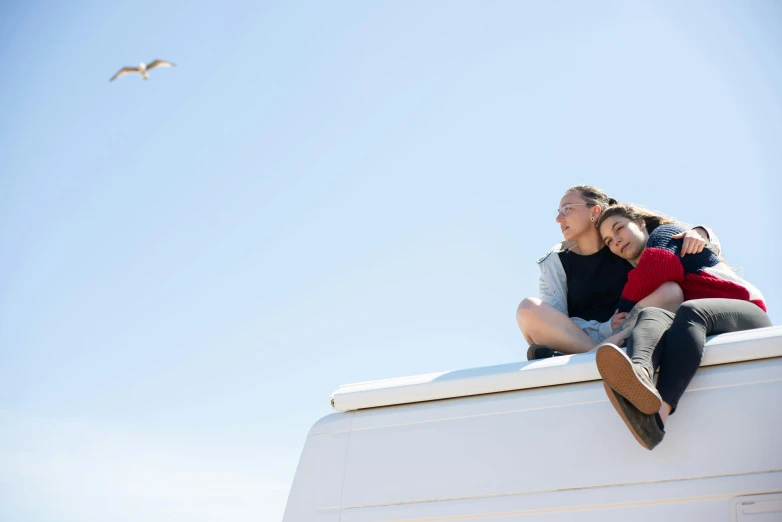 a man and a woman sitting on top of a van, birds overhead, seaview, family friendly, cuddling