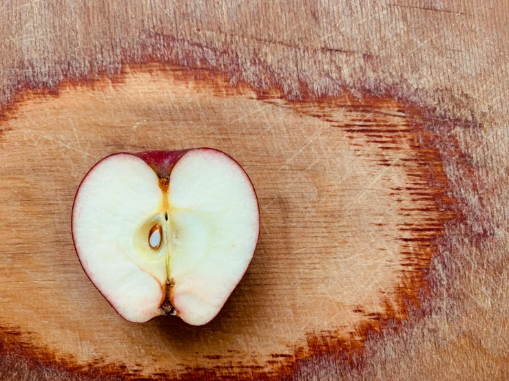 an apple cut in half on a wooden cutting board, by Jan Rustem, pexels, small heart - shaped face, semi-transparent, reddish, viewed from above