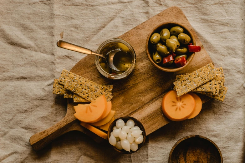 a wooden cutting board topped with cheese and olives, a still life, inspired by Ceferí Olivé, pexels, honey, background image, pickle, snacks