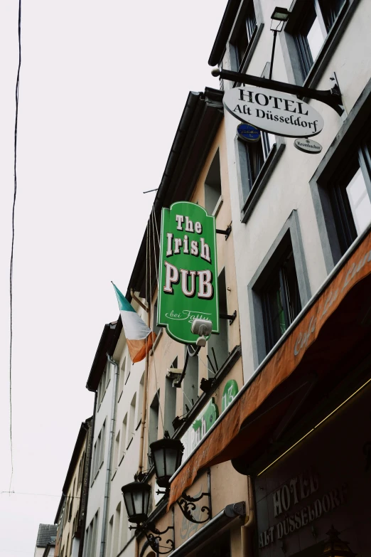a green sign hanging from the side of a building, a photo, unsplash, art nouveau, a pint of beer sitting on a bar, irish, multiple stories, thumbnail