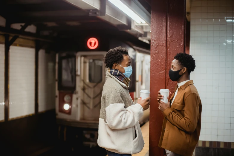 two people standing next to each other on a subway platform, by Carey Morris, trending on pexels, facemask, drinking a coffee, harlem, a cozy