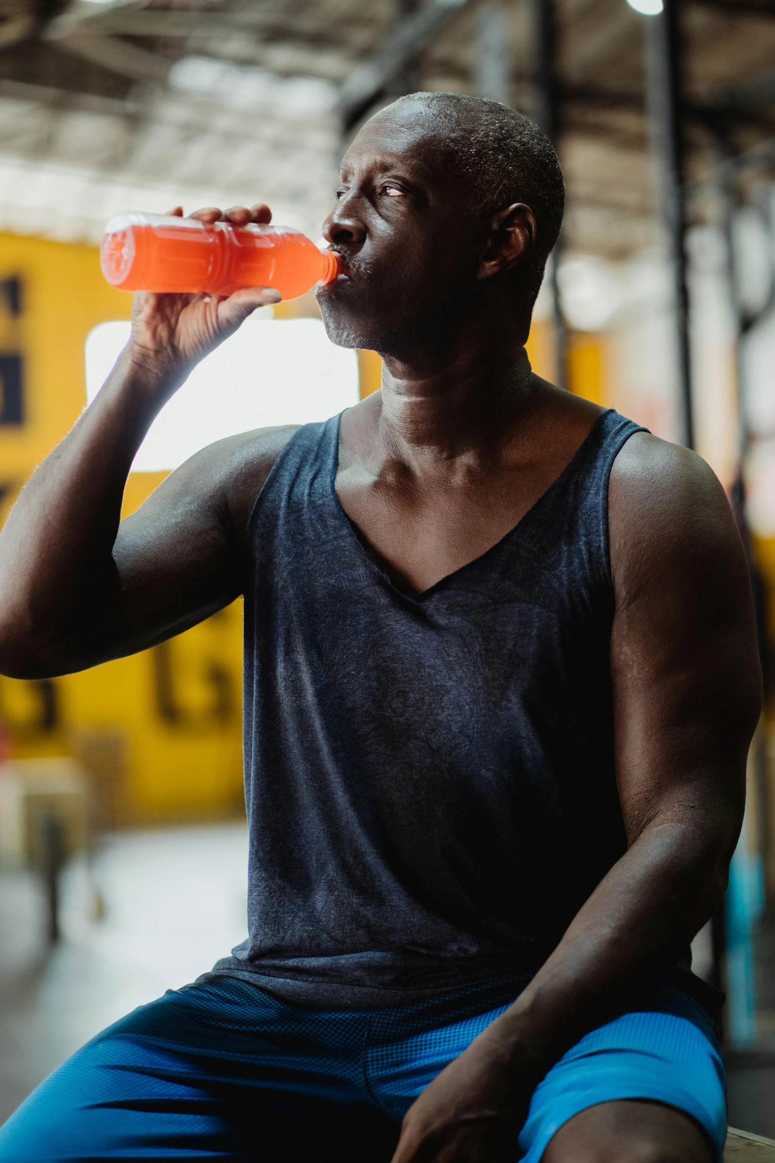 a man sitting on a bench drinking from a water bottle, pexels contest winner, wearing an orange t-shirt, man is with black skin, local gym, 🍸🍋